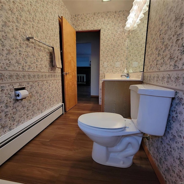 half bathroom featuring wallpapered walls, toilet, wood finished floors, and a baseboard heating unit