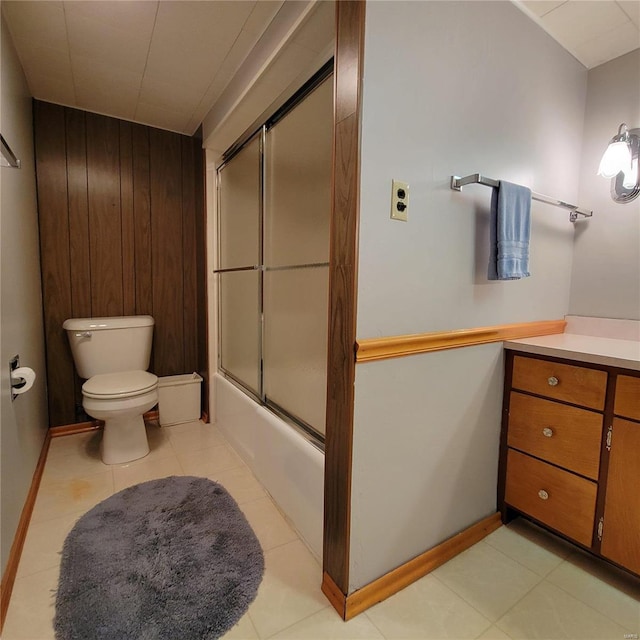 full bath featuring tile patterned flooring, wooden walls, toilet, enclosed tub / shower combo, and vanity