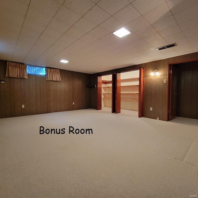 basement featuring visible vents, carpet, and wood walls