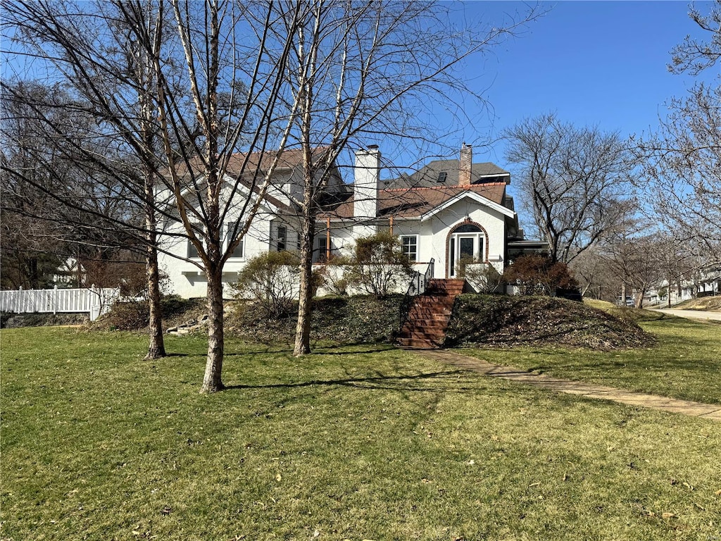 view of side of property with stucco siding, a lawn, a chimney, and fence