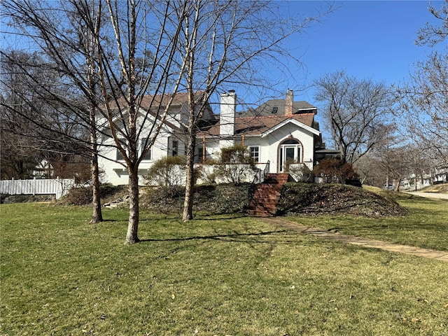 view of side of property with stucco siding, a lawn, a chimney, and fence