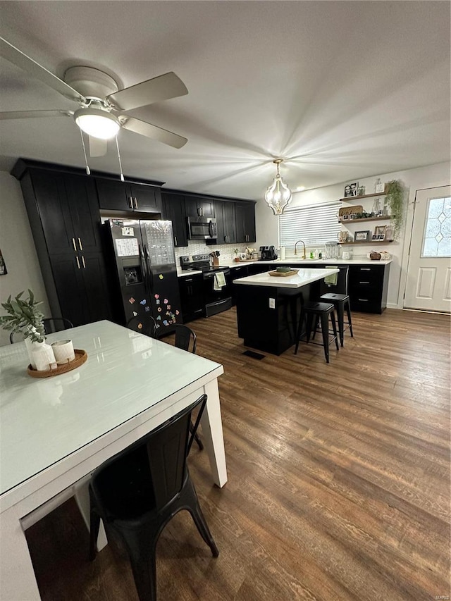 kitchen with dark hardwood / wood-style floors, decorative light fixtures, a breakfast bar area, a center island, and black appliances