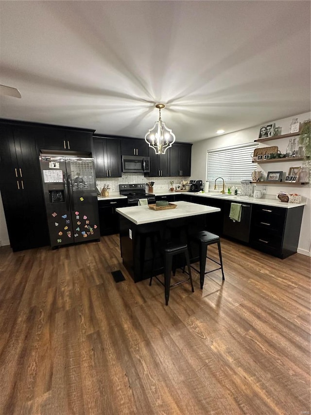 kitchen with a breakfast bar, a center island, black appliances, dark hardwood / wood-style flooring, and decorative light fixtures