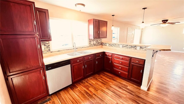 kitchen with pendant lighting, sink, stainless steel dishwasher, kitchen peninsula, and light hardwood / wood-style flooring