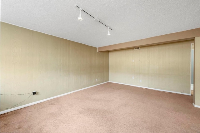 carpeted empty room with a textured ceiling, baseboards, and track lighting