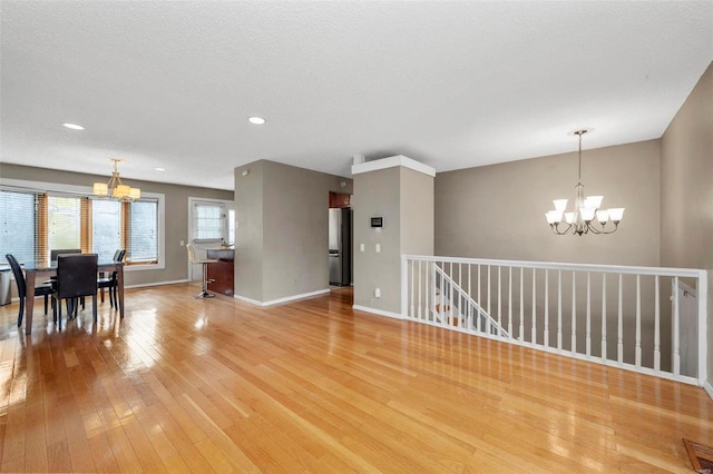 empty room with a chandelier, light wood-type flooring, a textured ceiling, and baseboards