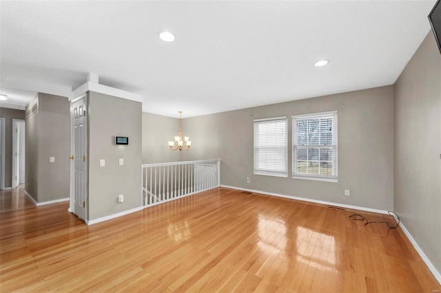 empty room featuring baseboards, recessed lighting, light wood-type flooring, and an inviting chandelier