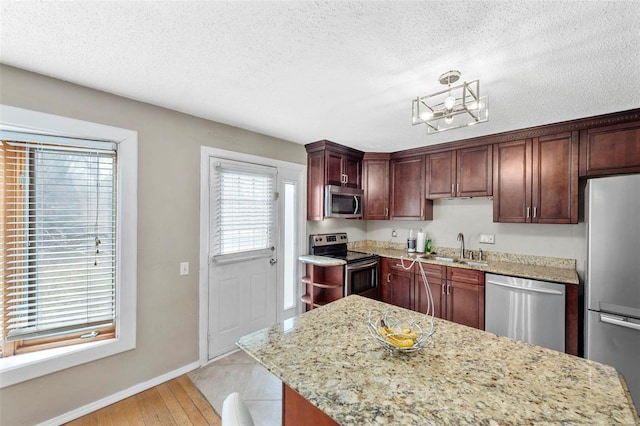 kitchen with a textured ceiling, appliances with stainless steel finishes, a sink, and light stone counters