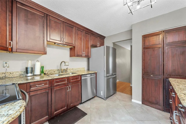 kitchen with a textured ceiling, light stone counters, a sink, dark brown cabinets, and appliances with stainless steel finishes