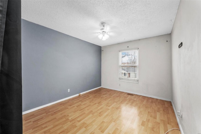 empty room featuring a textured ceiling, wood finished floors, a ceiling fan, visible vents, and baseboards