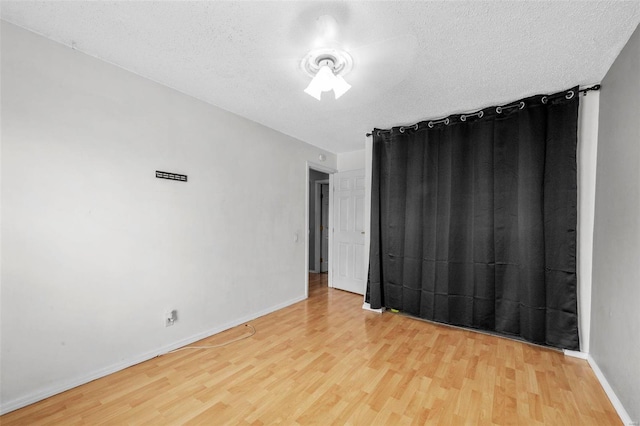 empty room with a textured ceiling, baseboards, and wood finished floors