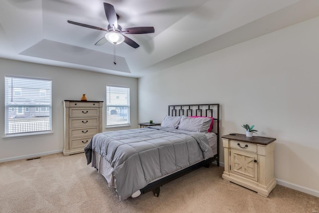 bedroom featuring a tray ceiling, light colored carpet, and ceiling fan