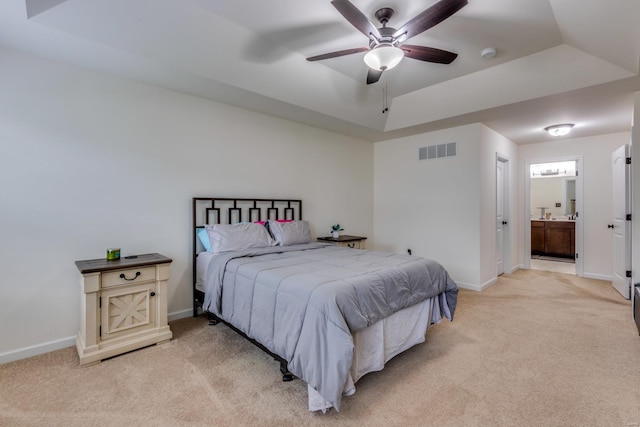 bedroom featuring ceiling fan, light colored carpet, ensuite bathroom, and a raised ceiling