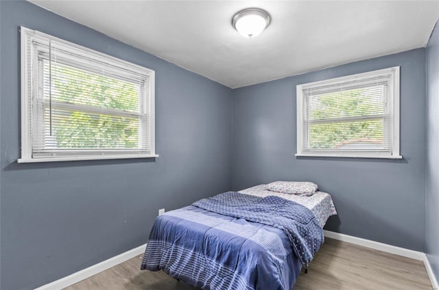 bedroom with multiple windows, baseboards, and wood finished floors