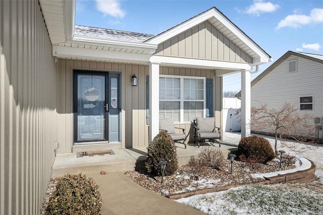 snow covered property entrance with board and batten siding, roof with shingles, and covered porch