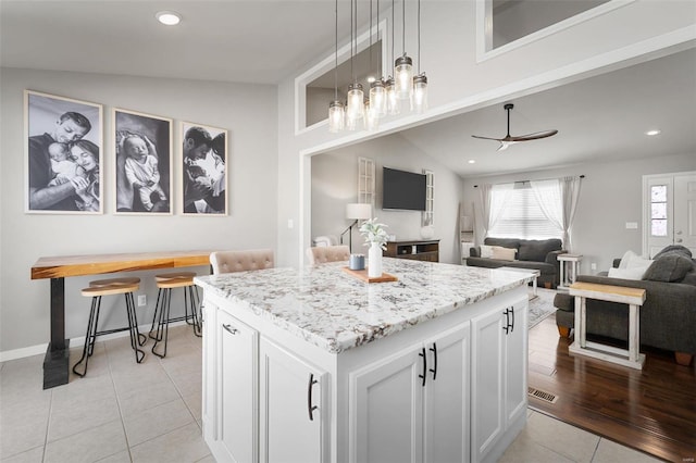 kitchen with lofted ceiling, open floor plan, a center island, white cabinetry, and light tile patterned floors