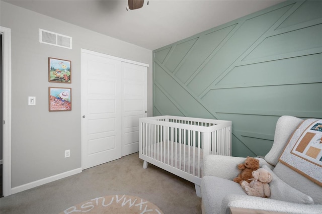 carpeted bedroom featuring ceiling fan, visible vents, a crib, baseboards, and a closet