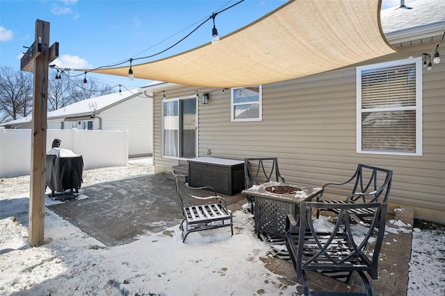 snow covered patio with an outdoor fire pit, fence, and area for grilling