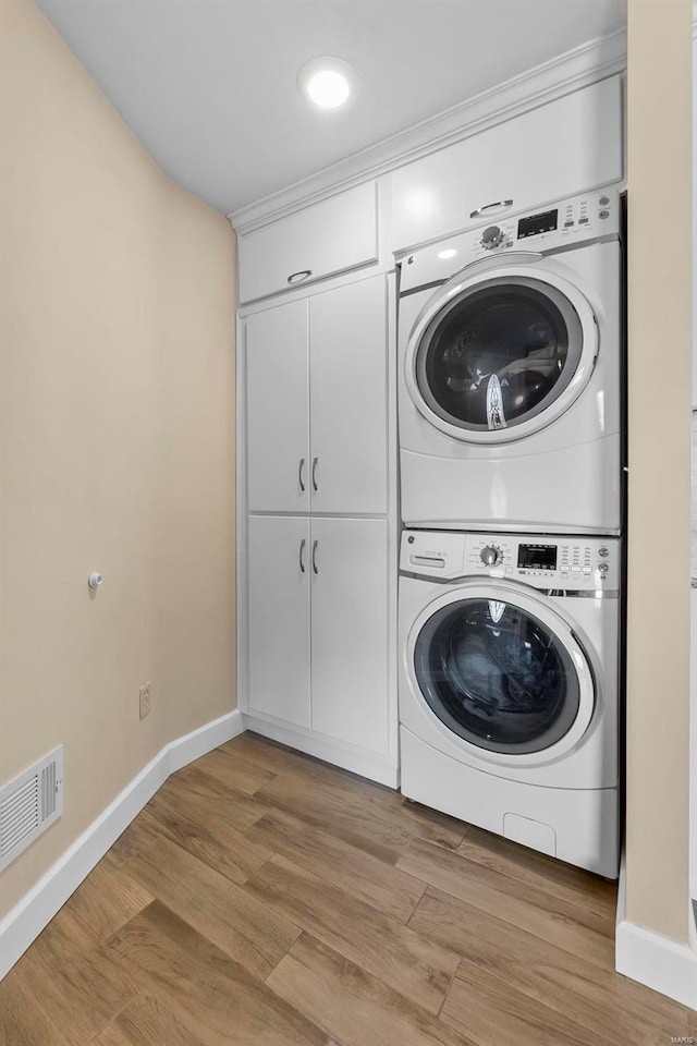 laundry room featuring stacked washer and dryer and light hardwood / wood-style flooring