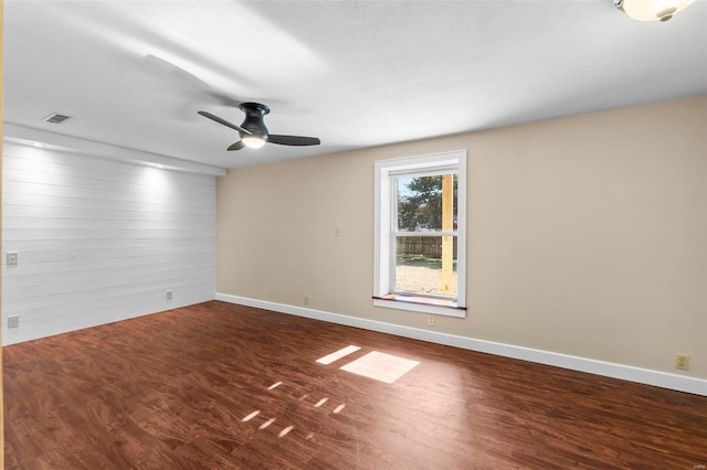 spare room featuring dark hardwood / wood-style floors, ceiling fan, and wood walls