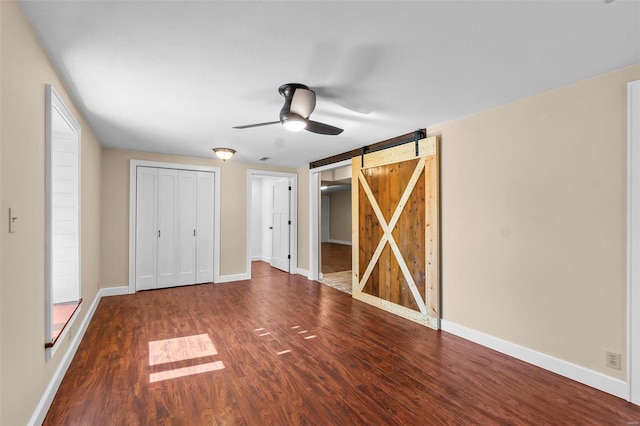 unfurnished bedroom with wood-type flooring, a barn door, and ceiling fan