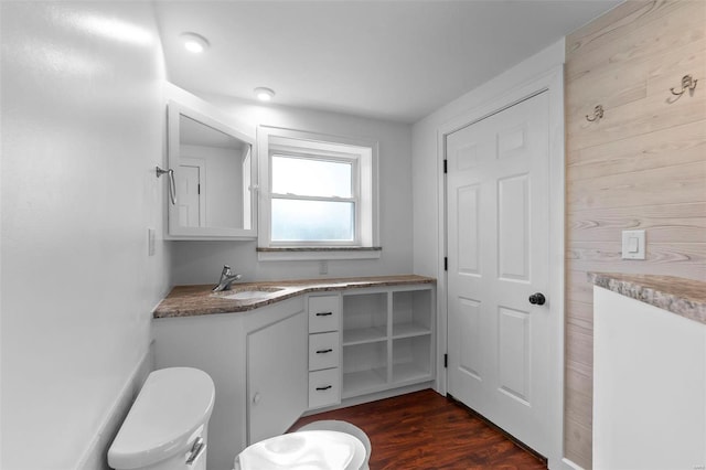 bathroom featuring vanity, hardwood / wood-style floors, wooden walls, and toilet