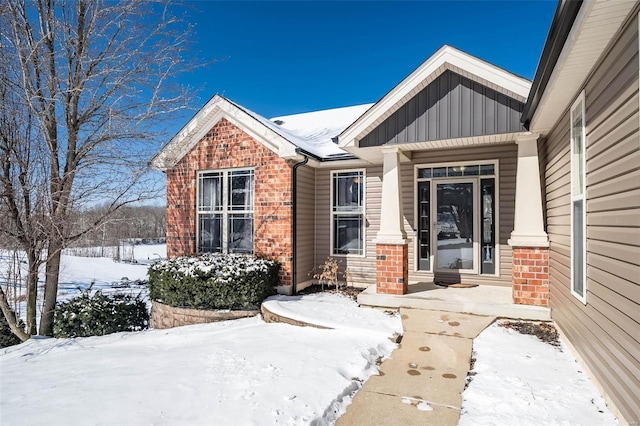 snow covered property entrance with brick siding and board and batten siding