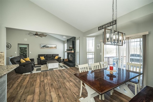 dining room featuring a fireplace, high vaulted ceiling, wood finished floors, and ceiling fan with notable chandelier