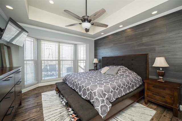 bedroom with an accent wall, a tray ceiling, dark wood-style flooring, and crown molding