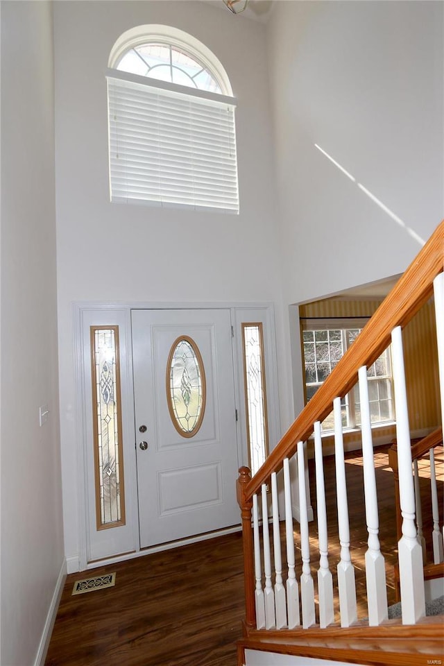 foyer entrance with stairway, visible vents, baseboards, dark wood-style flooring, and a towering ceiling