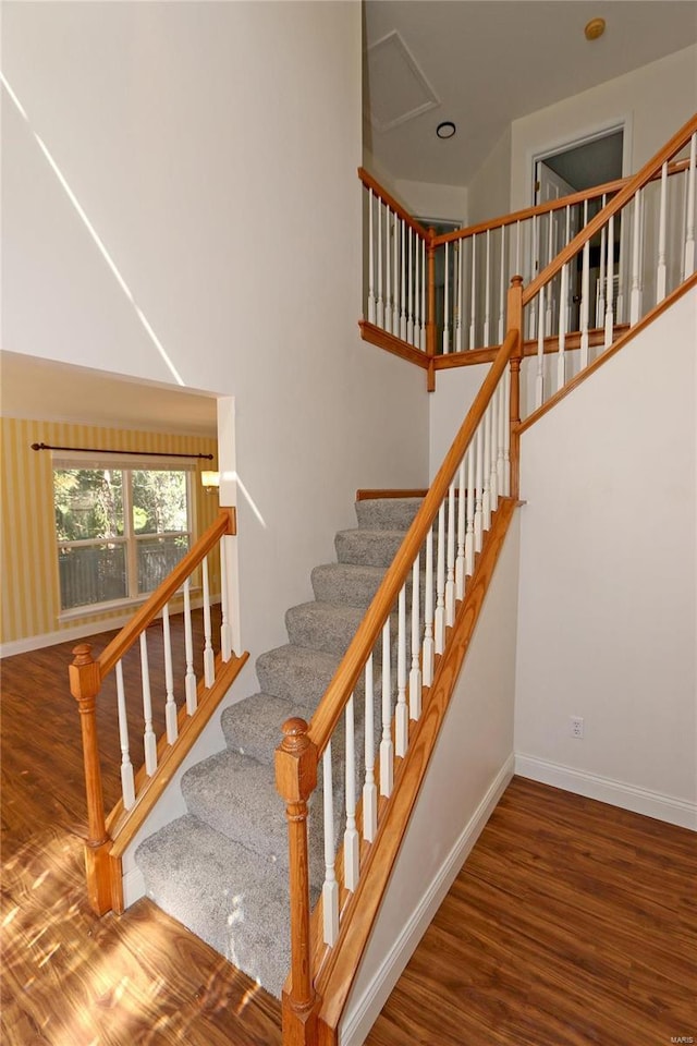 stairway with a high ceiling, wood finished floors, and baseboards