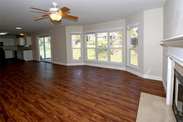 unfurnished living room with visible vents, ceiling fan, baseboards, a fireplace, and wood finished floors