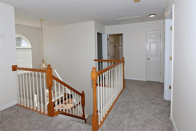 hallway featuring attic access, carpet flooring, an upstairs landing, and baseboards