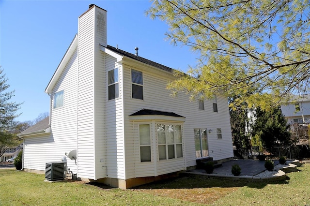 rear view of house with a lawn, cooling unit, a chimney, and a patio