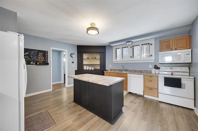 kitchen featuring white appliances, a sink, a kitchen island, light countertops, and light wood-type flooring