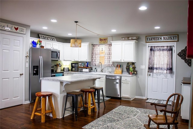 kitchen with appliances with stainless steel finishes, a kitchen breakfast bar, white cabinets, decorative light fixtures, and a kitchen island