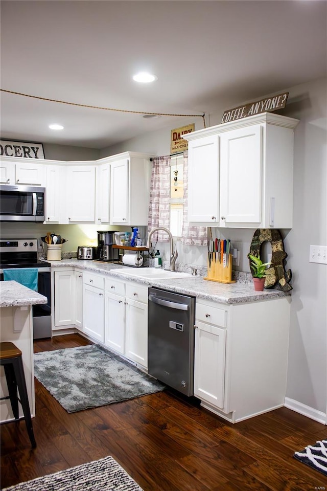 kitchen with white cabinetry, light stone countertops, sink, appliances with stainless steel finishes, and dark hardwood / wood-style floors