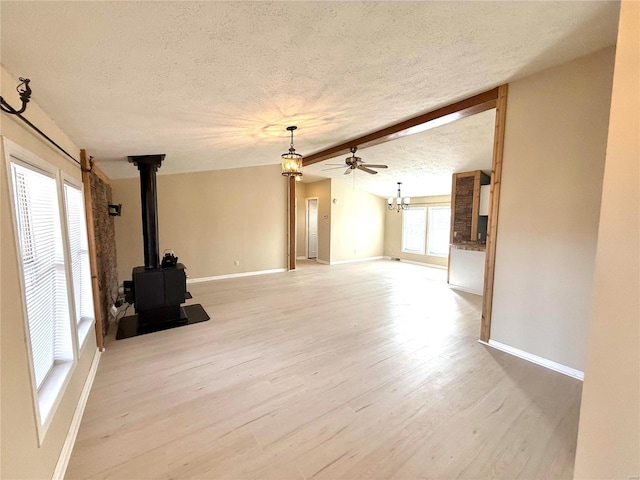 unfurnished living room with vaulted ceiling with beams, light wood-type flooring, a textured ceiling, and a wood stove