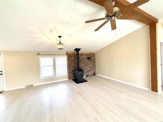 unfurnished living room featuring light hardwood / wood-style flooring, vaulted ceiling, ceiling fan, and a wood stove