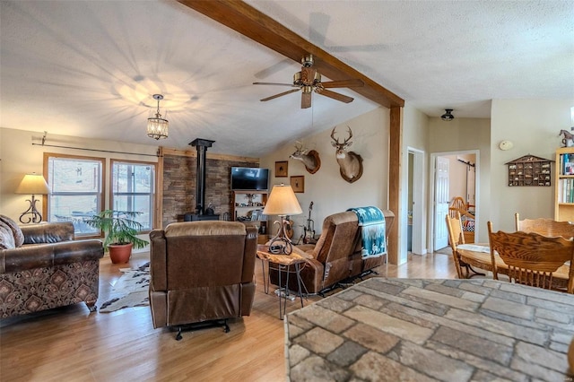 living room with ceiling fan, lofted ceiling with beams, light hardwood / wood-style floors, a textured ceiling, and a wood stove