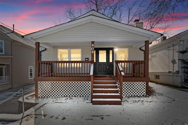 back house at dusk featuring a porch