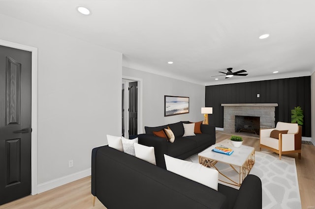 living room with ceiling fan, a stone fireplace, and light hardwood / wood-style floors