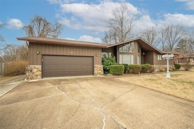 mid century modern featuring stone siding, driveway, and a garage