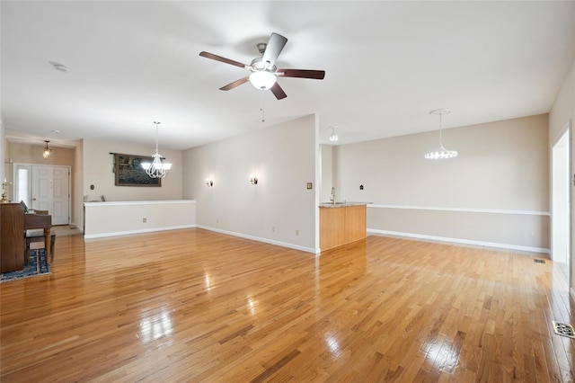 unfurnished living room featuring a sink, baseboards, light wood-style flooring, and ceiling fan with notable chandelier