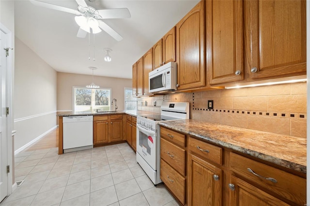 kitchen featuring a sink, stone countertops, backsplash, white appliances, and brown cabinetry