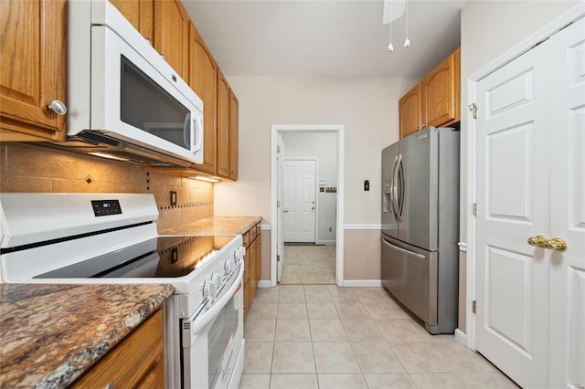 kitchen featuring brown cabinets, white appliances, light tile patterned floors, decorative backsplash, and baseboards