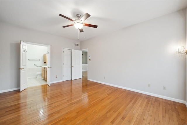 unfurnished bedroom featuring light wood finished floors, visible vents, connected bathroom, baseboards, and ceiling fan with notable chandelier