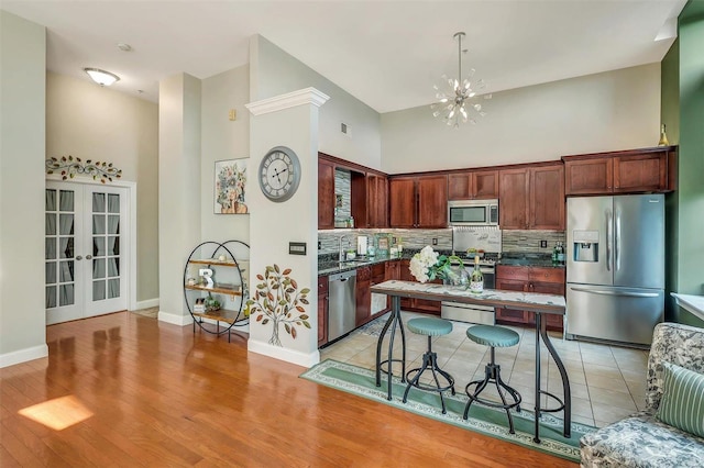 kitchen with a chandelier, decorative backsplash, a high ceiling, stainless steel appliances, and french doors