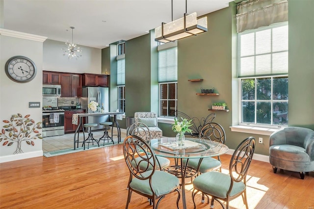 dining area featuring an inviting chandelier, ornamental molding, light hardwood / wood-style flooring, and a high ceiling