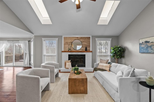 living area with light wood finished floors, lofted ceiling with skylight, ceiling fan, and a brick fireplace